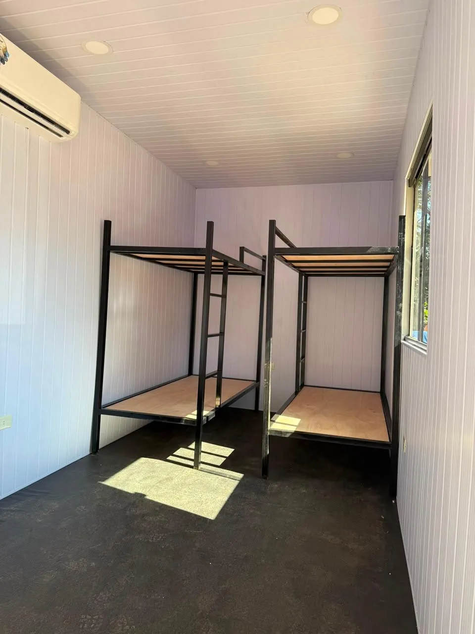 Dormitorio con dos literas metálicas enfrentadas y revestimiento PVC blanco