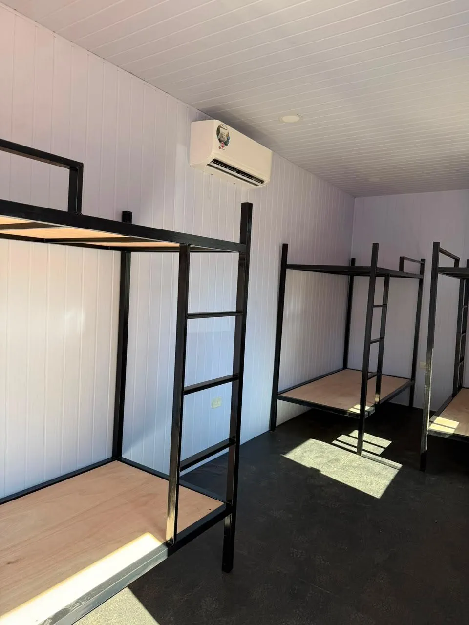 Dormitorio grande con varias literas metálicas, PVC acanalado y aire acondicionado