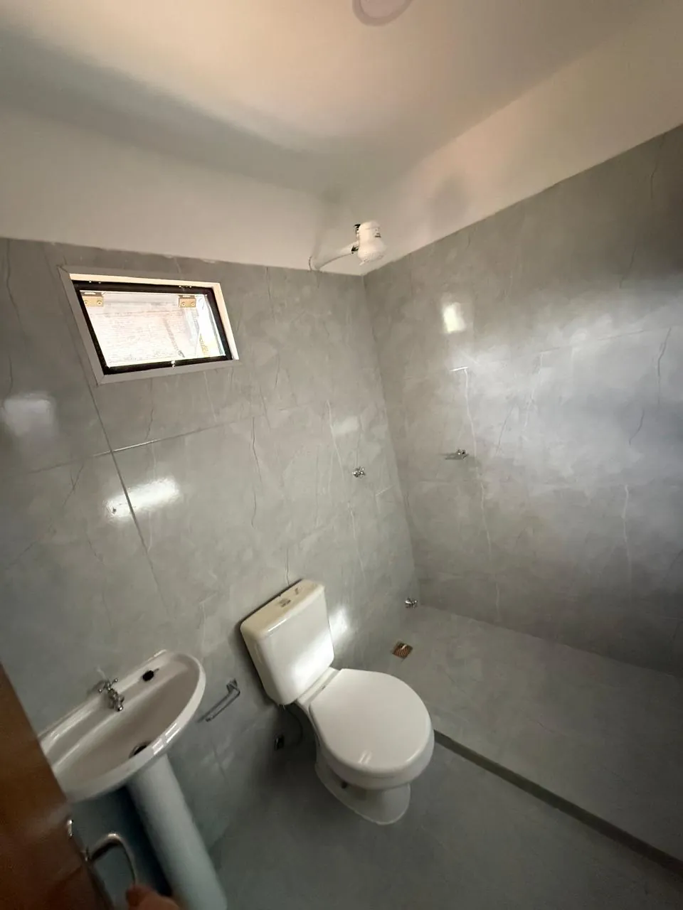 Baño del módulo con revestimiento gris, inodoro, vanitory y ventana de ventilación