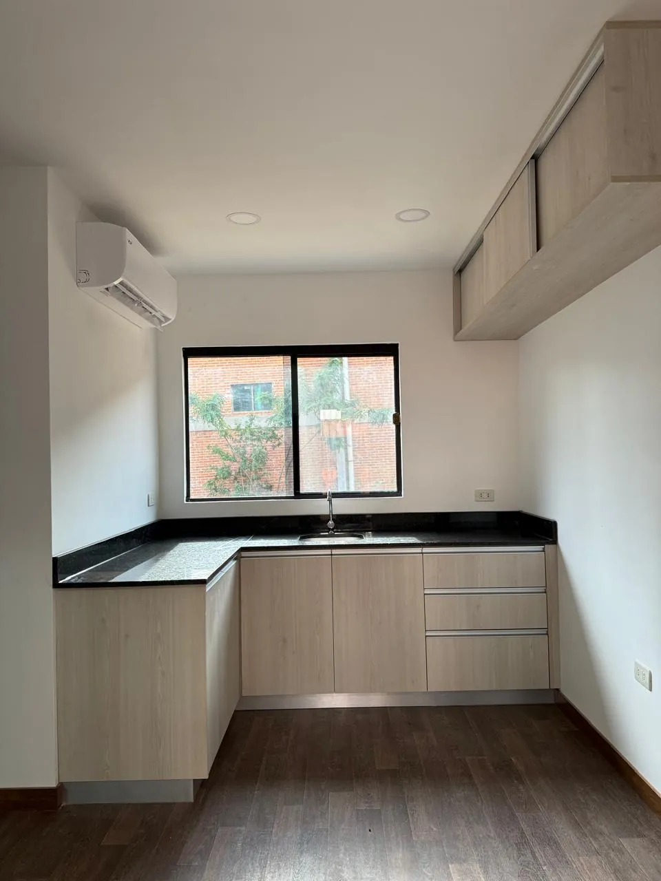 Kitchenette en L con mesada de granito negro, bacha de acero inoxidable y muebles bajomesada