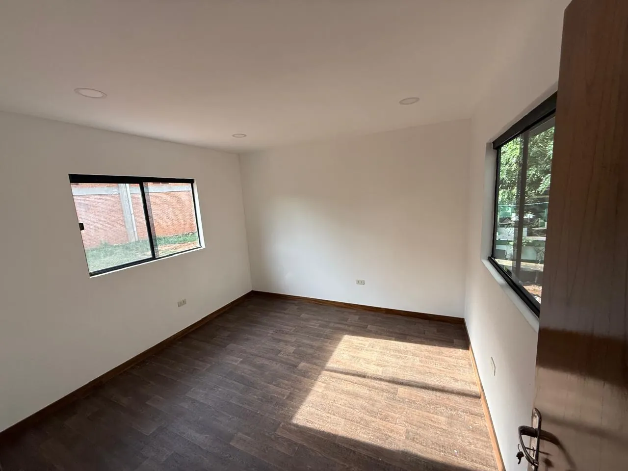 Oficina interior con piso vinílico símil parquet y dos ventanas de marco negro