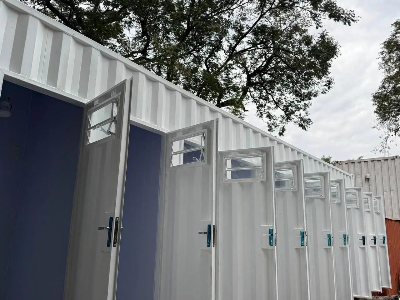 Fachada lateral del módulo sanitario con fila de puertas individuales y ventanas basculantes