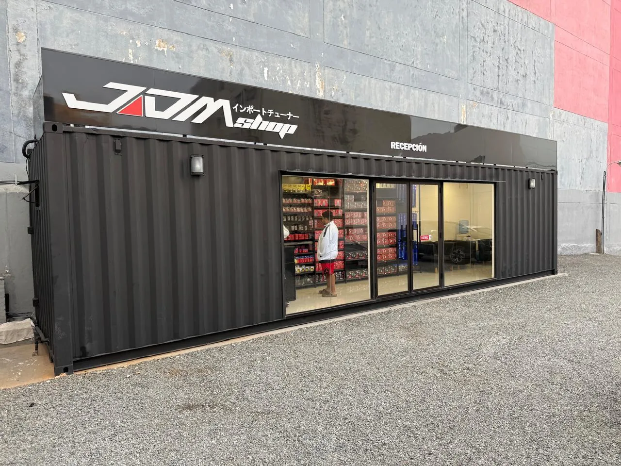 Showroom en contenedor de 40 pies con frente vidriado y banda superior negra, fachada frontal