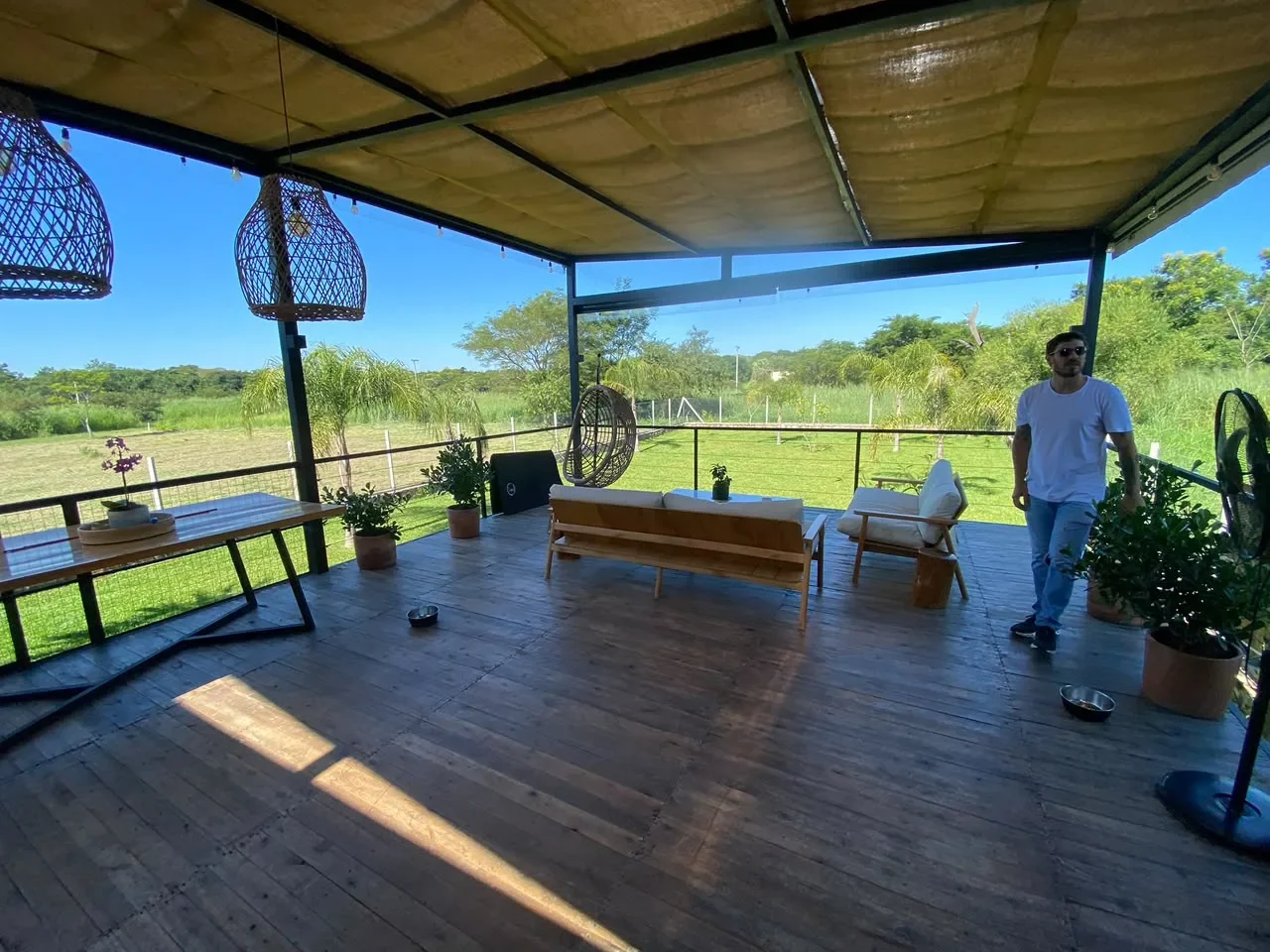 Quincho con deck de madera, techo de cana y sillas huevo colgantes, con vista abierta al campo.