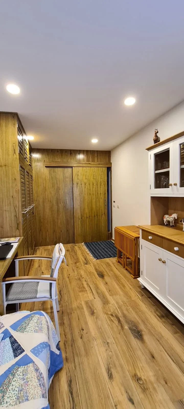 Interior de casa de contenedor con placares de enchapado de madera, piso de madera, aparador blanco y caballito de bronce, deco calida con patchwork azul.