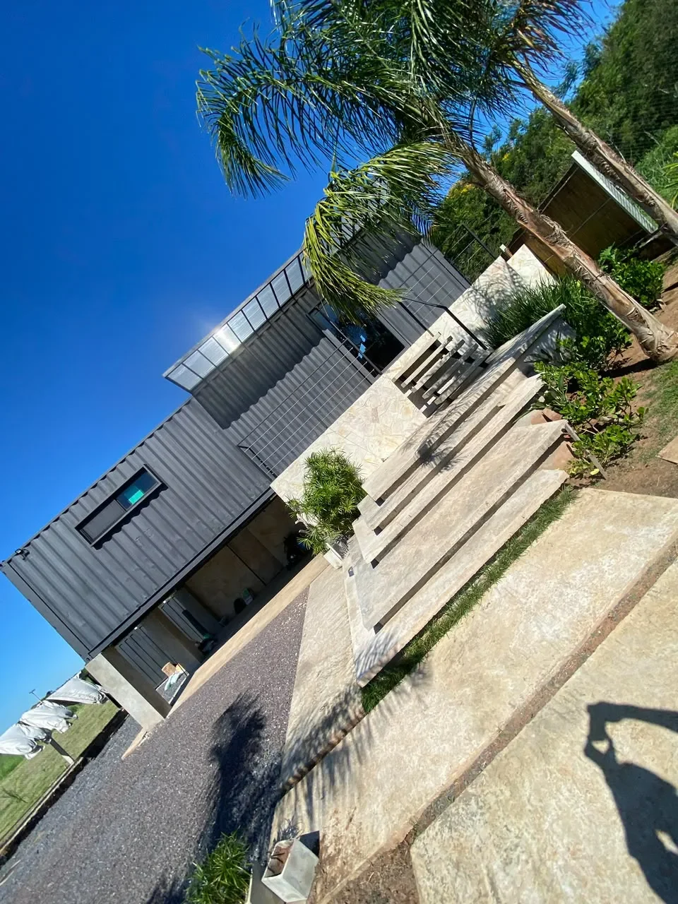 Casa de lujo gris de dos plantas en contenedor, toma en contrapicado de la escalera de hormigon y la palmera.