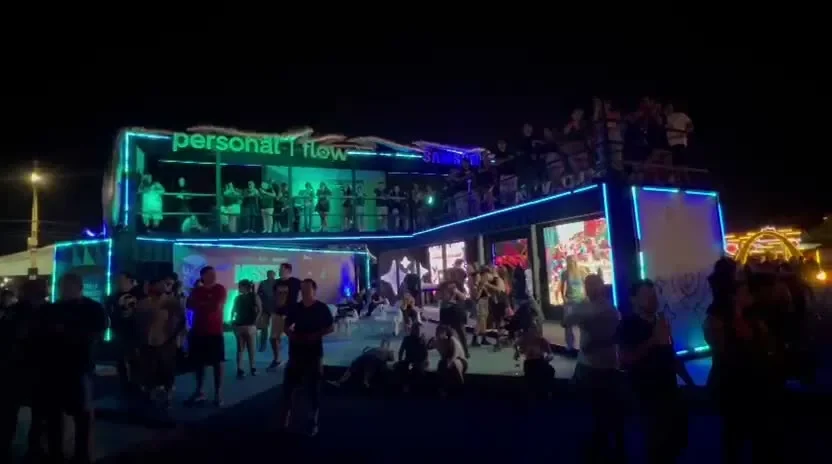 Toma panoramica nocturna del showroom de dos plantas en contenedor de Personal Flow y Samsung en Mission Rock, con LED y publico.